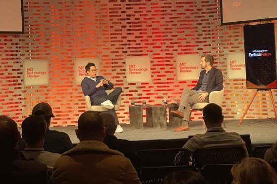 Jerry Chow, left, sits next to and speaks to James O'Donnell, sitting to the right, on a stage with 'MIT Technology Review' signs on the wall behind them. 