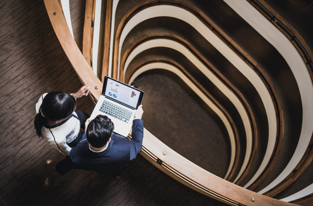 Two businesspeople at the top of a computer looking at data on a computer.